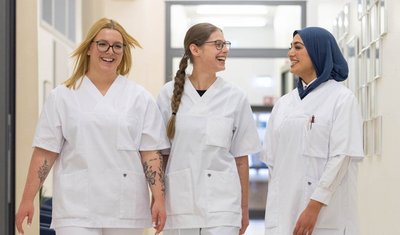 Drei Pflegeschülerinnen gehen gemeinsam über einen Gang.